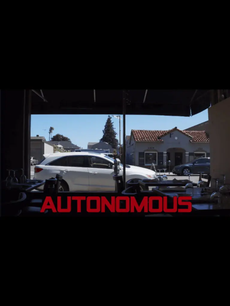 A white autonomous car sits outside storefronts, seen from indoors, with "AUTONOMOUS" and Old Bat Films in bold red at the bottom.